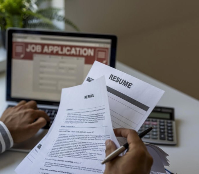A recruiter comparing printed resumes against an on-screen job application